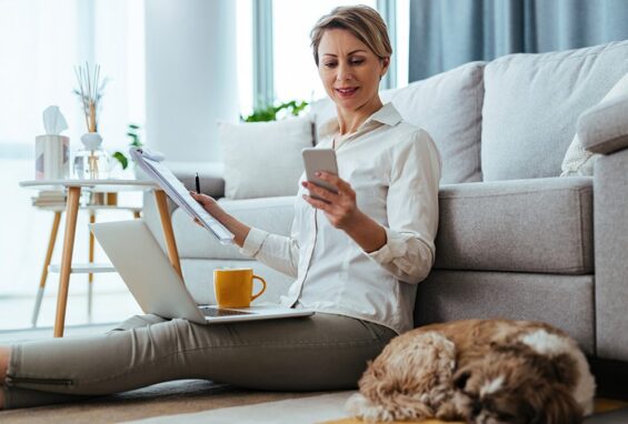 Young businesswoman texting on smart phone while sitting on the floor and working at home. Her dog is sleeping next to her.