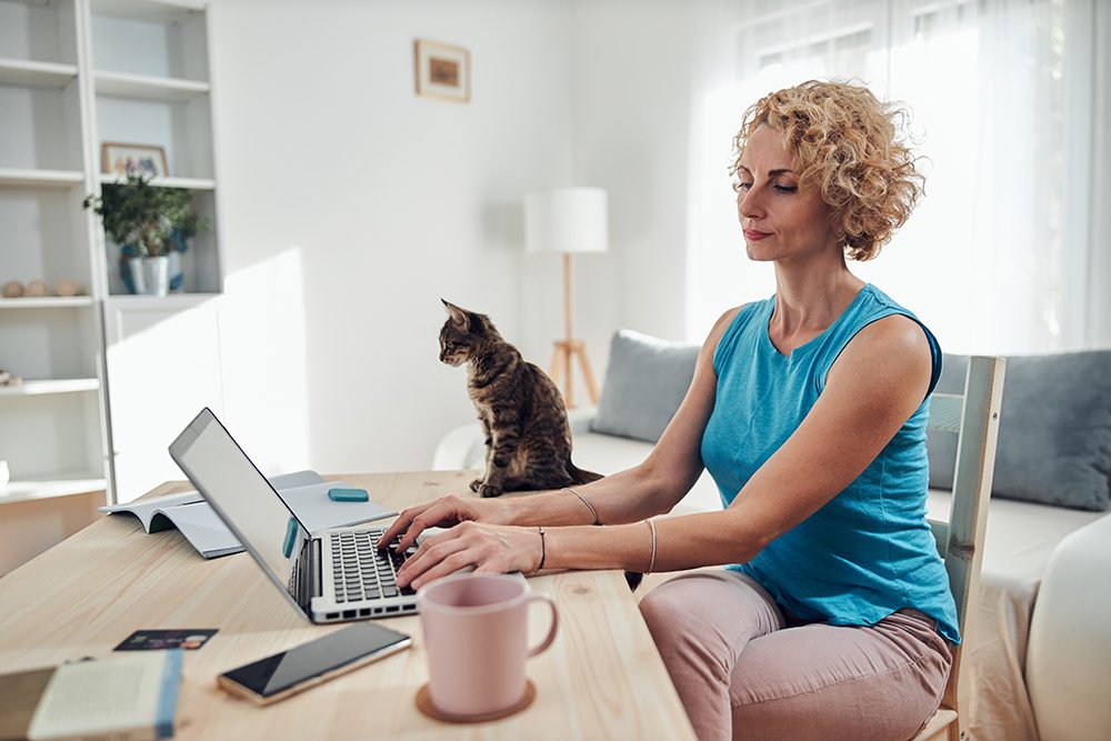 Woman working from home on a laptop / notebook with cat pet with her.